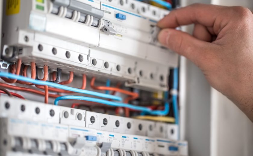 Man, an electrical technician working in a switchboard with fuses. Installation and connection of electrical equipment. Professional with tools in hand. concept of complex work, space for text.